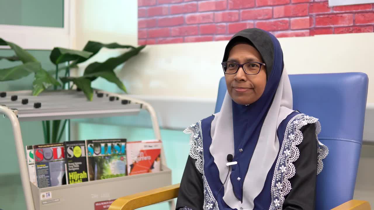 Malaysian woman called Sheila sitting in a chair wearing a hijab and a microphone telling her story